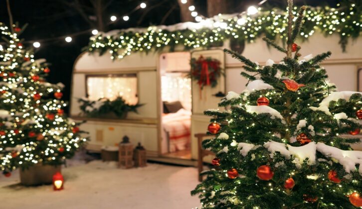 A caravan covered in Christmas decorations, beside a Christmas tree